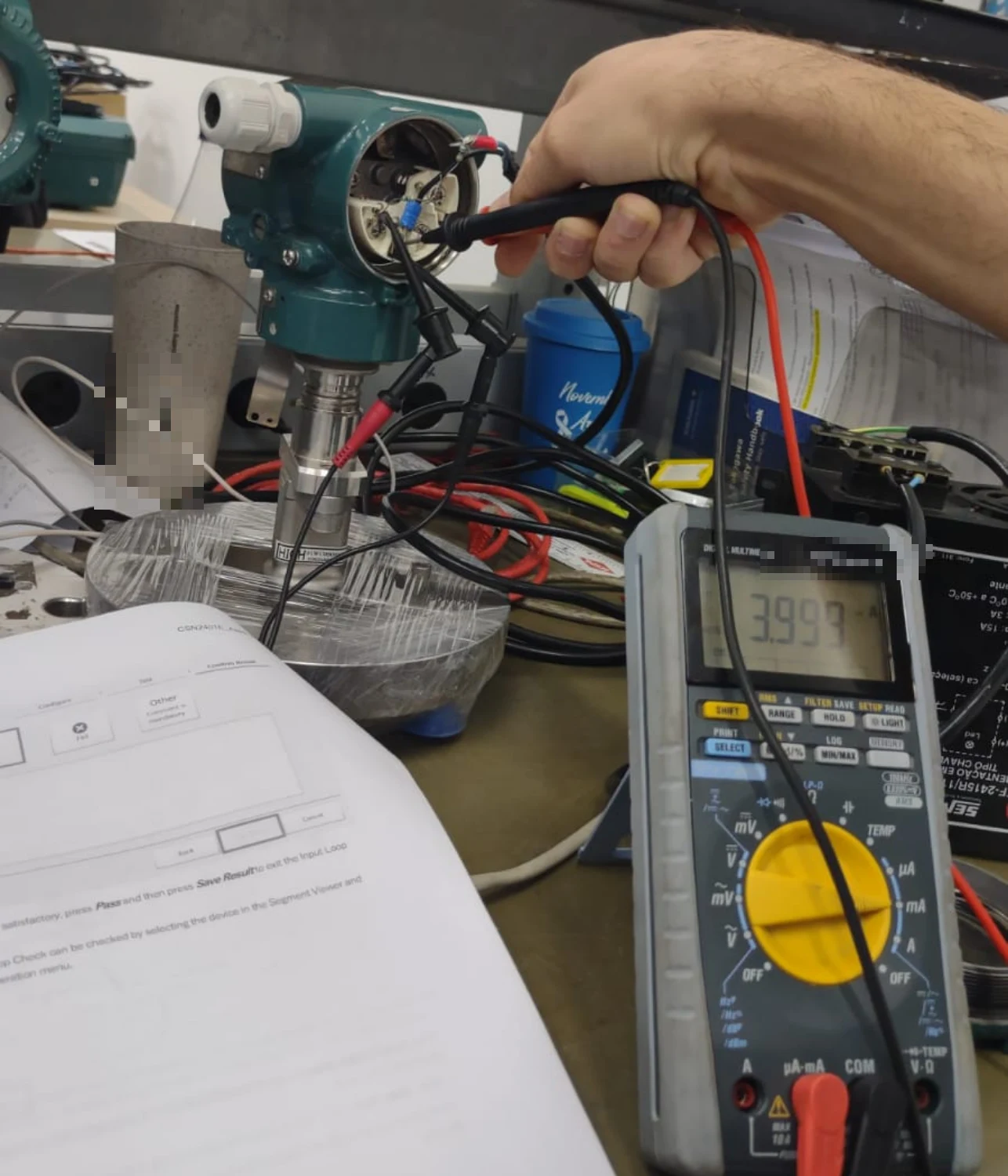 Técnico realiza teste de malha em transmissor de pressão com multímetro, em bancada de instrumentação.