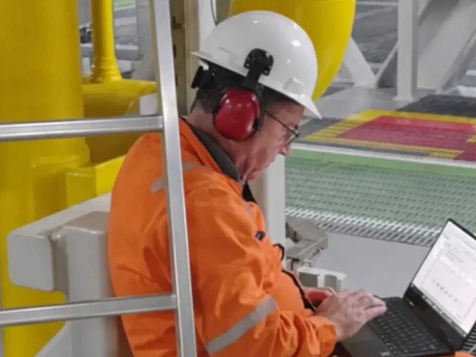Técnico com EPI completo em notebook durante atendimento de campo em unidade industrial.