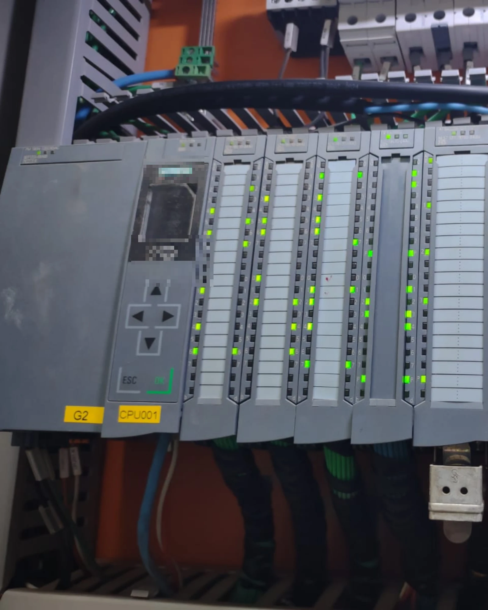 Rack de CLP com módulos de entrada e saída em operação, indicadores luminosos acesos, em painel industrial.